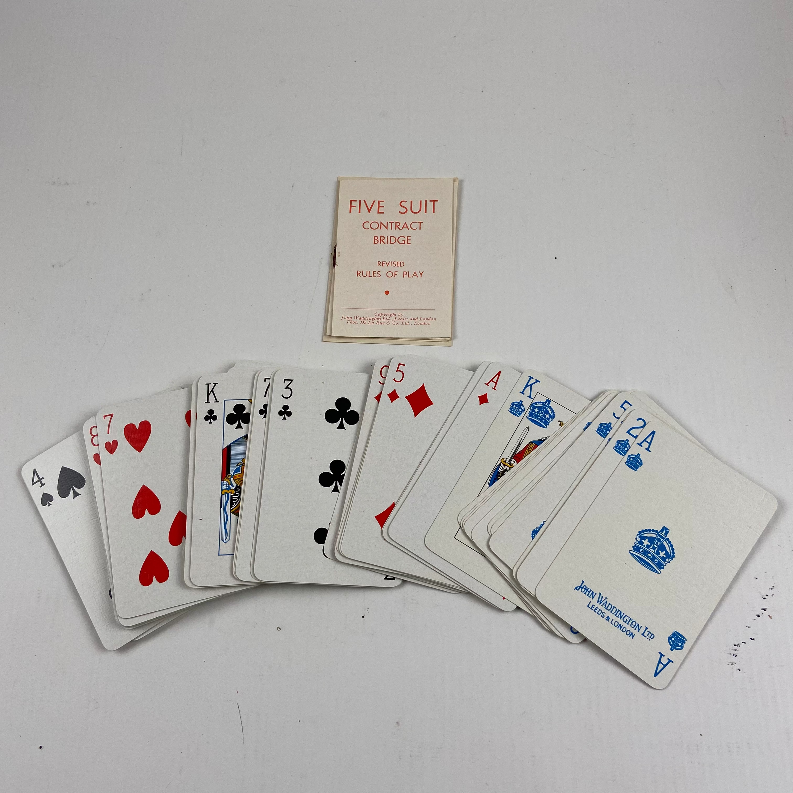 Playing cards spread out on a white surface with a small box labeled 'Five Suit Contract Bridge' in the background.